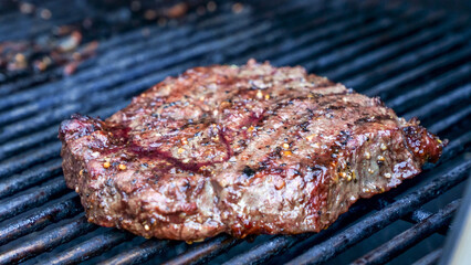 Grilled meat steak on stainless BBQ grill with flames on dark background. Food and cuisine concept.