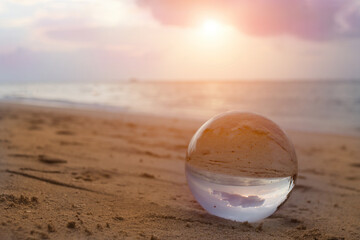 Beautiful scenic view through lens of crystal ball on water horizon at summer sunset. Clouds...