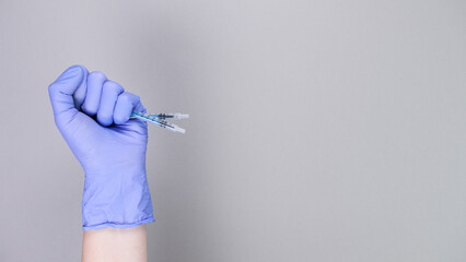 Hand in blue gloves of doctor or nurse holding syringe with liquid vaccine over grey background...