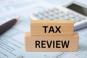Tax review text on wooden blocks with tax form and calculator background. Taxation concept