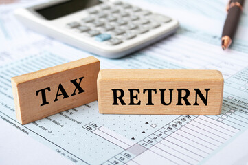 Tax return text on wooden blocks with tax form and calculator background. Taxation concept