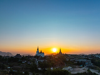 Naklejka premium Aerial view amazing Big White Five buddha Statues in Wat Phra Sorn Kaew temple. .The sun shone on the edge of the mountain, casting a golden glow on the ornate statue. .Stands elegantly on the hill.
