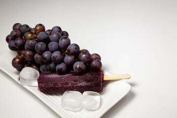 Grape stick popsicle with grapes on top, on a white plate with ice. Slightly blurred image on the side. Summer concept.