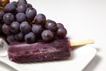 Grape stick popsicle with grapes on top, on a white plate with ice. Slightly blurred image on the side. Healthy summer concept.