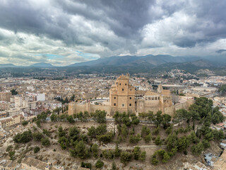 Fototapeta na wymiar Aerial view of Caravaca de la Cruz castle dominating the landscape with square and circular towers, medieval palace and Baroque ornament facade church