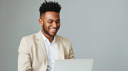 Smiling Businessman Using Laptop.A cheerful young man in a beige blazer working on a laptop, enjoying his work in a bright office environment.
