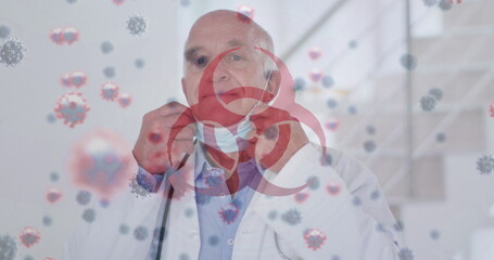 Biohazard symbol and covid-19 cells floating against male senior doctor lowering his face mask
