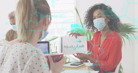 Image of digital interface showing statistics with colleagues in office wearing face masks
