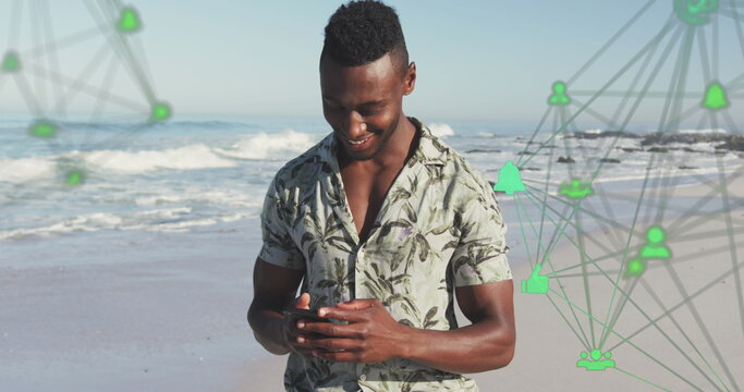 Image of spinning networks with social media digital icons over man using smartphone on beach