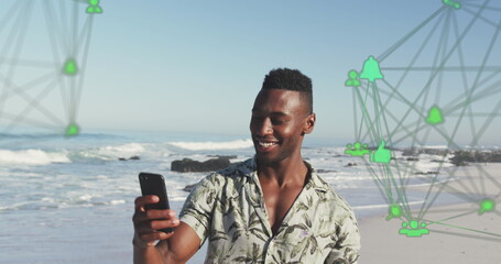 Image of spinning networks with social media digital icons over man using smartphone on beach