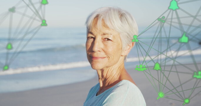 Image of network of connections with icons over smiling senior woman on beach