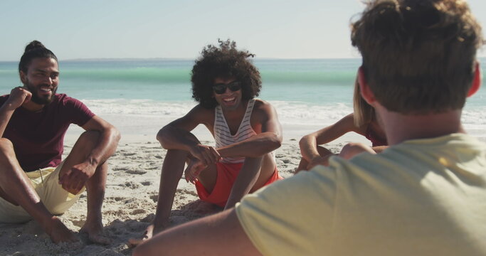 Young biracial man and friends enjoy a sunny beach day, with copy space
