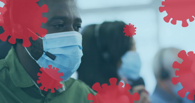 Image of floating covid-19 cells icons with colleagues in office wearing face masks