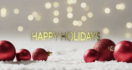 Happy holidays text with glittery red christmas baubles on snow and bokeh lights background