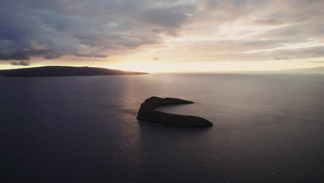 Amazing slow aerial shot through clouds over the Pacific ocean with Molokini Crater and the sacred island of Kaho'olawe in the distance during amazing sunset on Maui, Hawai'i. .