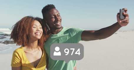 Profile icons with increasing numbers against african american couple taking a selfie on the beach - Powered by Adobe