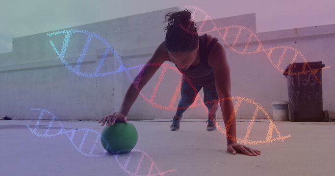 Image of dna strands spinning over woman doing press ups, exercising with ball in gym - Powered by Adobe