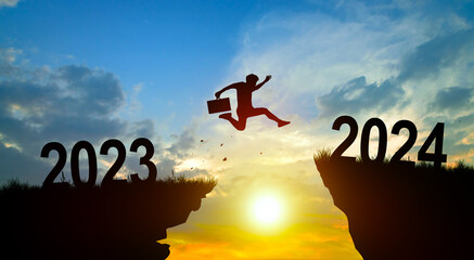 Welcome merry Christmas and Happy new year in 2024. Man jumping across the gap from 2023 to 2024 cliff with Sunset and Twilight Sky background.