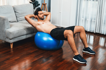 Athletic and sporty man doing situp on fitness ball during home body workout exercise session for...
