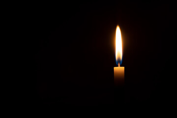 A single burning candle flame or light glowing on an orange candle on black or dark background on table in church for Christmas, funeral or memorial service with copy space