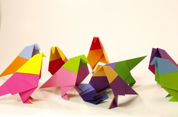 Side angle view of several origami birds in various postures around and on top of another origami...