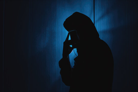 Dark silhouette of a mysterious Scammer in a hoodie holding a phone, symbolizing secretive communication or illegal activity.