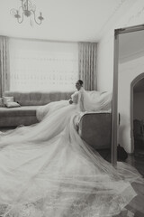 Young brunette in long wedding dress and veil in hotel room. A charming bride, full length, in a magnificent white dress on the morning before the wedding.