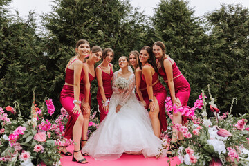 A brunette bride and her bridesmaids in matching pink dresses are standing near the solemn arch....