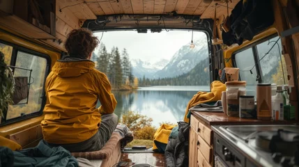  Tranquil van life scene with person gazing at a serene mountain lake from a cozy camper interior. Perfect for adventure and travel themes. © Tirawat