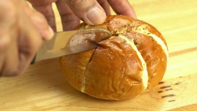 Man using kitchen knife cutting homemade korean cream cheese garlic bread on wooden cutting board.