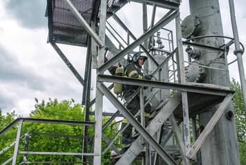 The rescuer climbs the stairs to the technological column during the accident. A firefighter in protective clothing and breathing apparatus during the liquidation of an accident at a chemical plant.