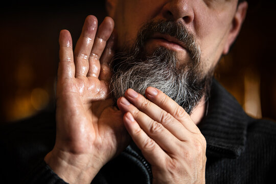 Grey bearded man applying beard oil or serum, care treatment at morning routine
