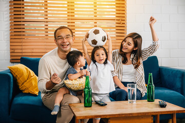 With popcorn in hand, a family and their daughter enjoy watching football on TV, fostering...