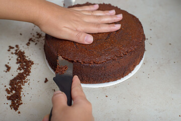 Person leveling a cake with a knife. Undecorated chocolate cake on wooden table.