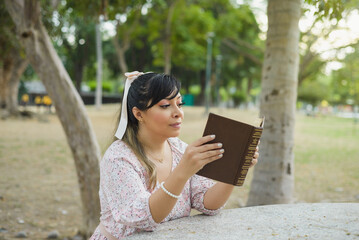 Fototapeta premium Woman sitting at a park table reading a book. World book day. Concept of reading.