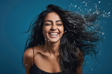 Studio portrait of a joyful young woman of Indian ethnicity having long flowing hair playing with water - obrazy, fototapety, plakaty
