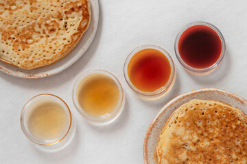 Different classes of maple syrups in different colours in glass bowls with pancakes next to them
