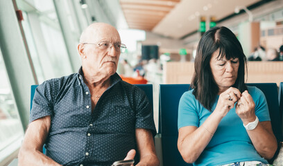 Angry senior couple ignoring each other sitting in airport departure area waiting for boarding.