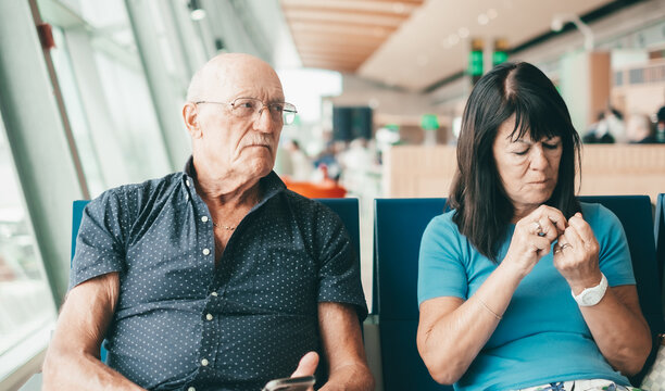 Angry Senior Couple Ignoring Each Other Sitting In Airport Departure Area Waiting For Boarding.