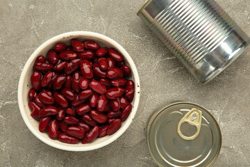 Red kidney beans in bowl and cans on grey background.