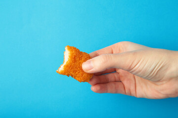 Chicken nugget with a bite taken in hand on a blue background