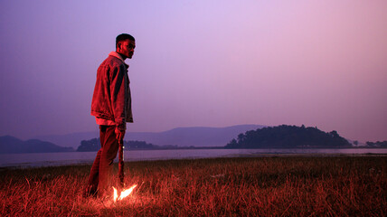 Image of brave man holding burning stick while moving in darkness. Young man holding a fire stick on the mountain top near the sea.  - Powered by Adobe