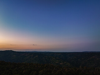 Aerial view A breathtaking sunset paints the sky with vibrant hues of orange and red, .casting a warm glow over the majestic mountains in a tranquil evening landscape.