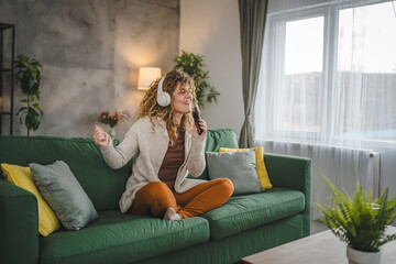 Obraz premium One woman with headphones at home listen music online happy smile sing