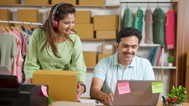 Joyful dancing couple working at ecommerce warehouse by wearing headphones - concept of workplace entertainment, small business owners and multitasking.