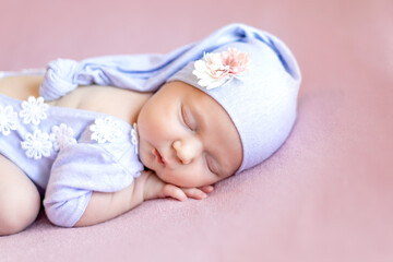 newborn baby girl in a blue bodysuit sleeping sweetly on her tummy in a cap on a pink background, close-up portrait