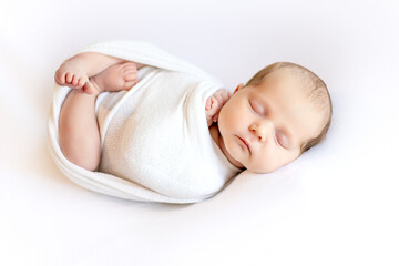 A newborn baby girl in a diaper cocoon is sleeping sweetly on a white isolated background