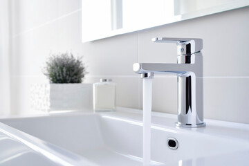 Modern white sink and faucet with flowing water, bright bathroom interior
