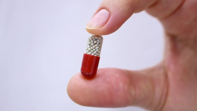 Female hand holding one medical capsule of nutritional supplement close up on white background