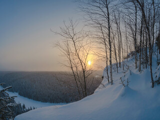 Beautiful sunrise on a frosty morning, a snowy cliff, trees on t